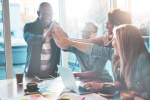 Foto eines Teams, das sich über den Tisch High-Five gibt | Diversity Management & Konflitmanagement